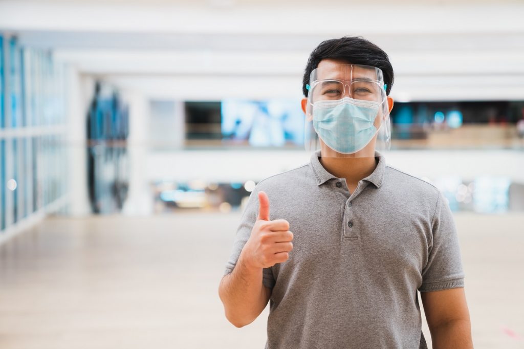 Young asian man wear face shield and mask smiling in shopping ma