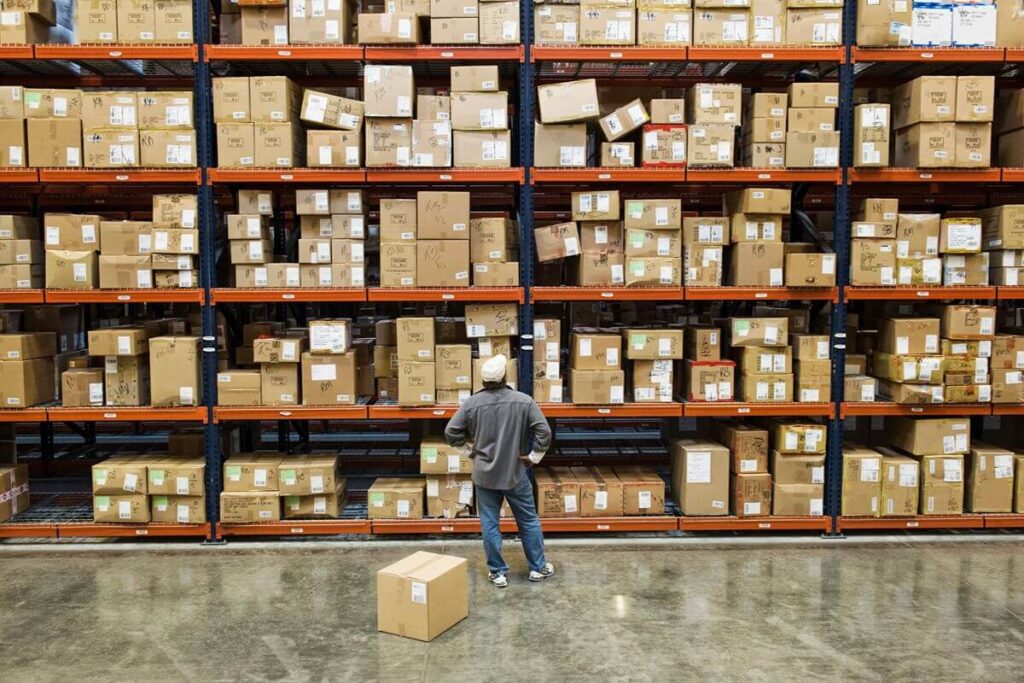Warehouse worker standing in front of shelves filled with labeled cardboard boxes and packaged inventory