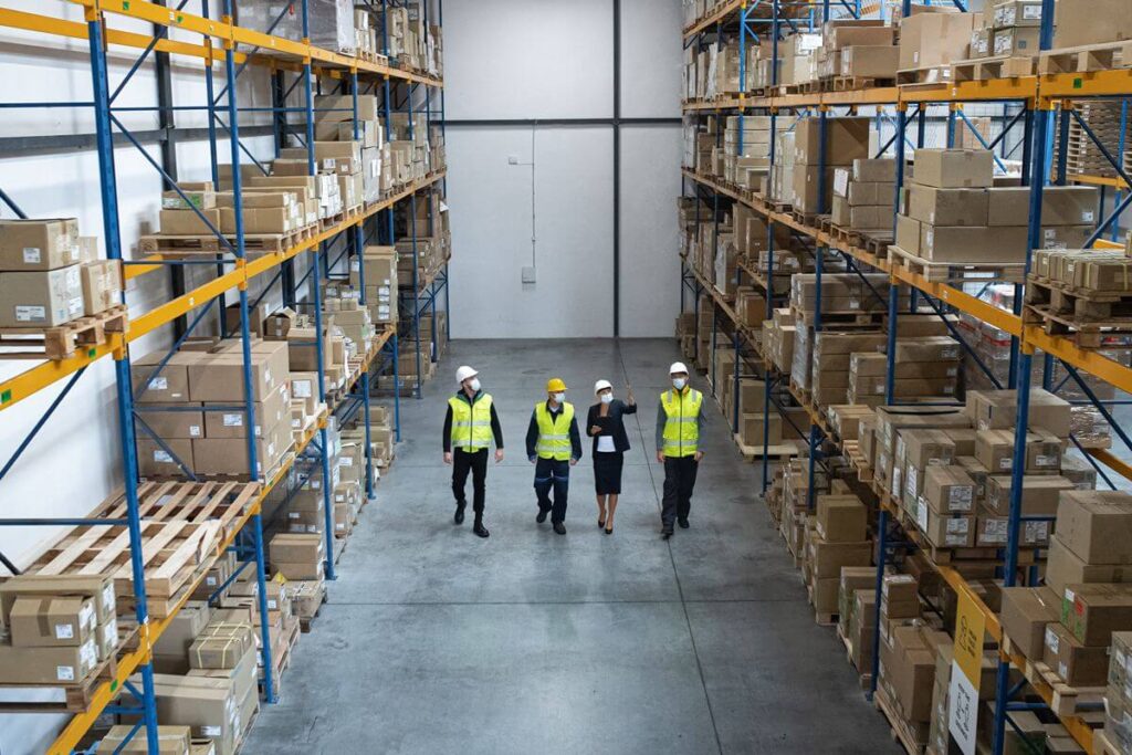Warehouse team walking through an organized storage facility lined with pallets and boxed inventory