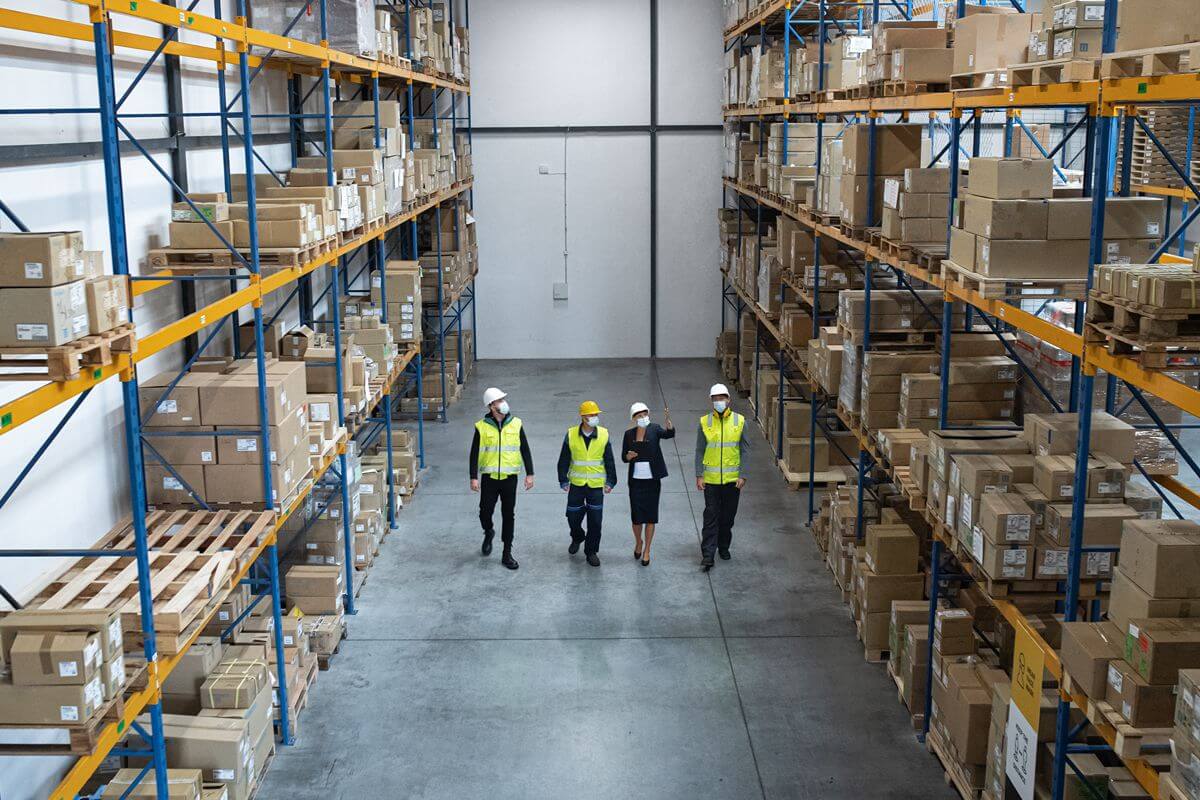 Warehouse team walking through an organized storage facility lined with pallets and boxed inventory